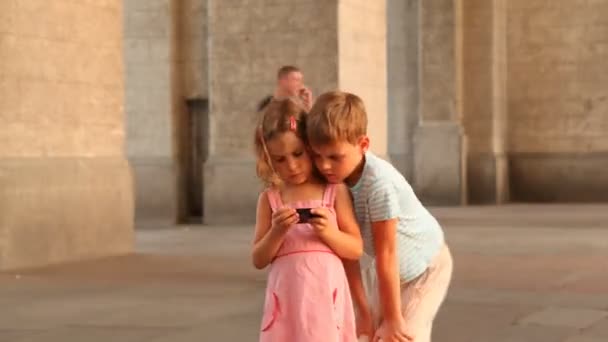 Kinder sind auf dem Platz und schauen sich Videos auf dem Smartphone an. — Stockvideo