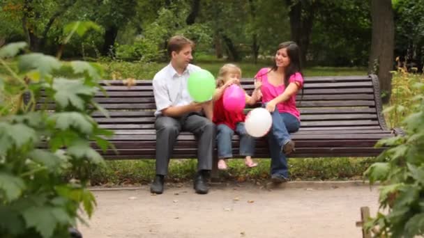 Семейная игра с воздушными шарами сидя на скамейке в парке — стоковое видео