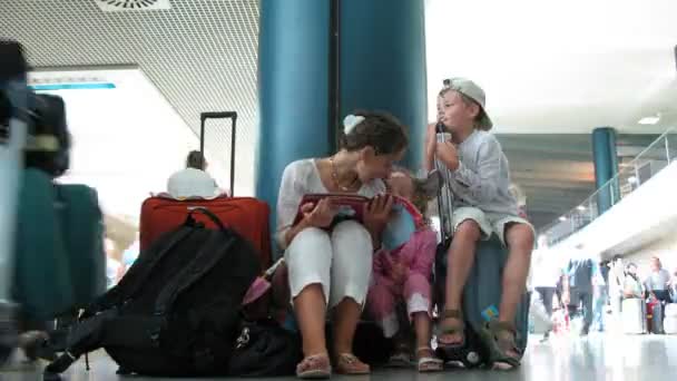 Madre con los niños se sientan sobre el equipaje en una sala del aeropuerto . — Vídeo de stock