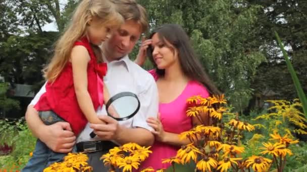 Chica y sus padres descubriendo la flor con lupa — Vídeo de stock