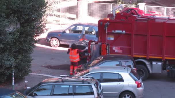 Два рабочих тащат мусорный бак в мусоровоз на улице — стоковое видео