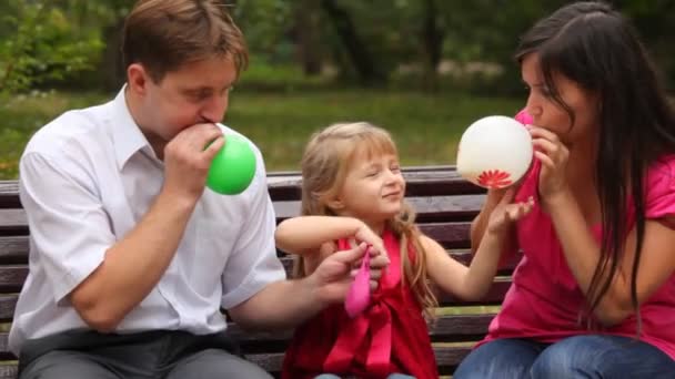 Family blow balloons sitting on bench in park — Stock Video