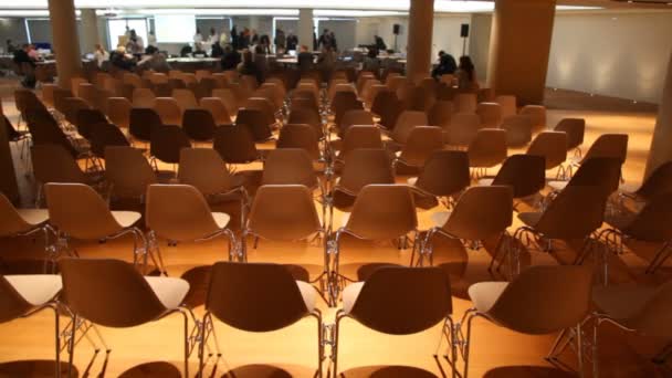 Algunos se mueven dentro de la sala de conferencias vacía de luz baja con muchas sillas — Vídeo de stock