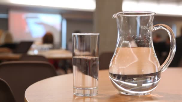 Cup and pitcher filled with water stand on table in conference hall — Stock Video