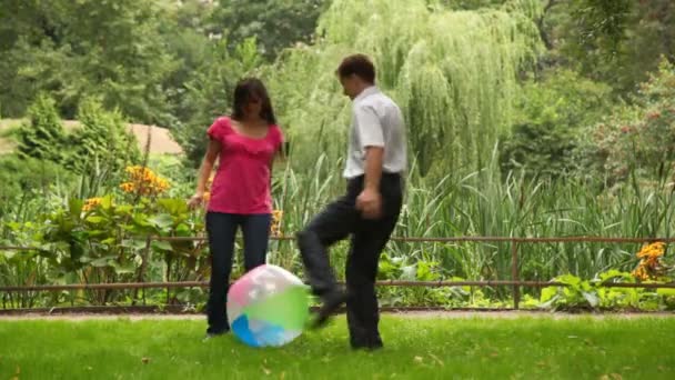 Couple kicks ball playing near fence in park — Stock Video