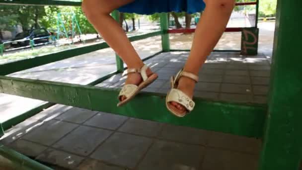 Маленькая девочка стоит на перилах беседки среди детских площадок — стоковое видео