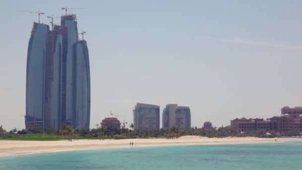 Κτίριο ουρανοξύστης κοντά παραλία με φοίνικες στο Αμπού Ντάμπι, Ηνωμένα Αραβικά Εμιράτα — Αρχείο Βίντεο