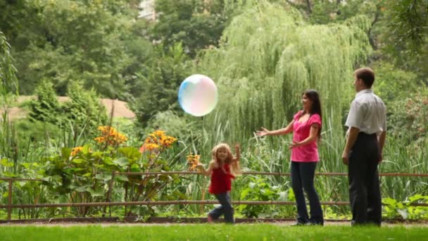 Couple play ball with daughter near fence in park — Stock Video