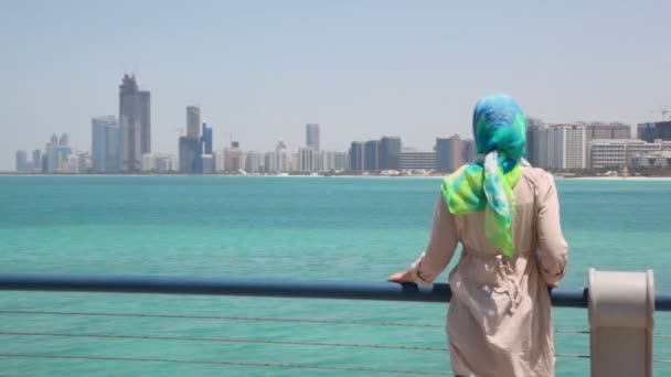 Mujer de pie en la orilla y mira los rascacielos en Abu Dhabi, Emiratos Árabes Unidos — Vídeo de stock
