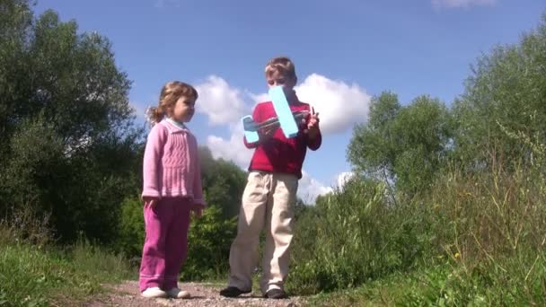 Klein meisje en jongen staan in park, jongen lancering speelgoed vliegtuig aanwezig. zonnige zomerdag. — Stockvideo