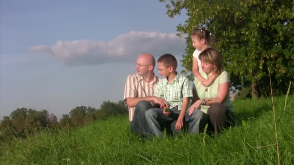 Family sits in a grass and looks afar. — Stock Video