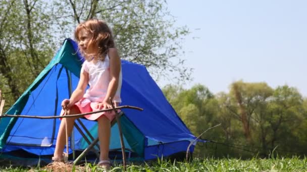 Niza niña se sienta en la silla con palo de madera en la mano cerca de la pequeña carpa azul en el día de verano bosque — Vídeo de stock