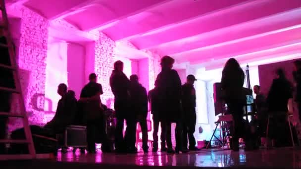 Люди заходят в комнату с розовым освещением во время съёмок видеоклипа — стоковое видео