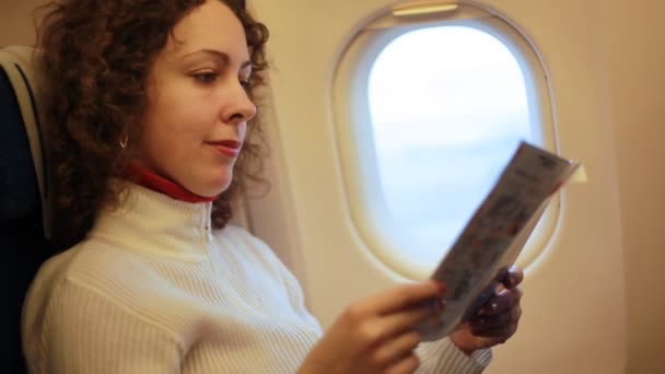 Женщина, сидящая в кресле самолета и читающая журнал — стоковое видео