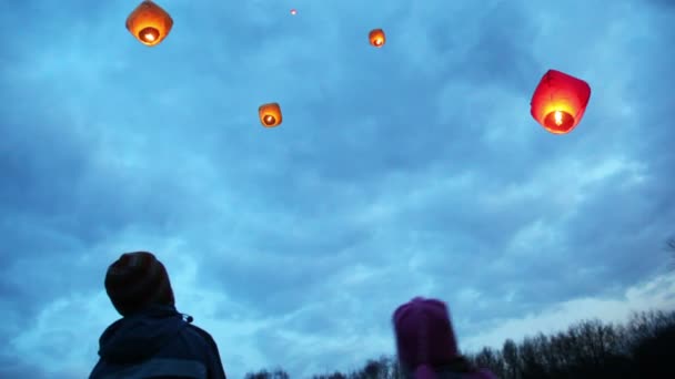 Junge und Mädchen schauen von unten nach oben auf fliegende chinesische Laternen — Stockvideo