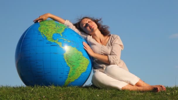 Cute girl sits relaxing in grass and rests on large inflatable ball at form of Earth against sky summer — Stock Video