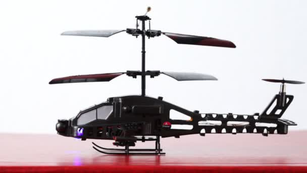 Toy helicopter is on table, its blades rotate, then flies up upwards, downwards and in front of chamber — Stock Video