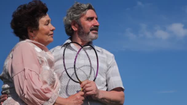 Здорова зріла пара з бадмінтоном влітку стоїть на тлі блакитного неба — стокове відео