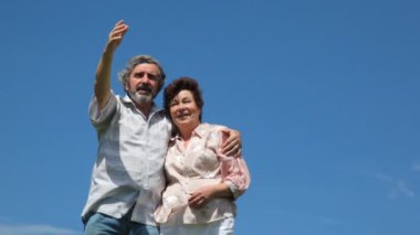 Olgun çift kucaklama standları, adam bir yere el gösterir ve eşi anlatıyor