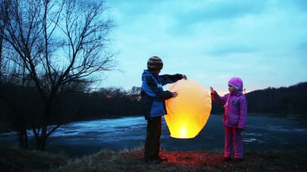 Хлопчик і дівчинка тримаються, ніжно торкаються китайського ліхтаря в зимовому лісі — стокове відео