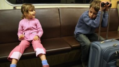 Çocuk oturur ve de çanta için eğilerek yatan kız kardeşi ona parmağını metro tren sürme gösterir