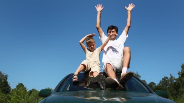 Father and son sitting on roof of car, then they waved with both hands — Stock Video