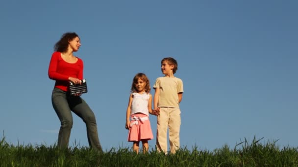 Мальчик и девочка стоят на траве, приходит их мать, нажмите клапперборд — стоковое видео