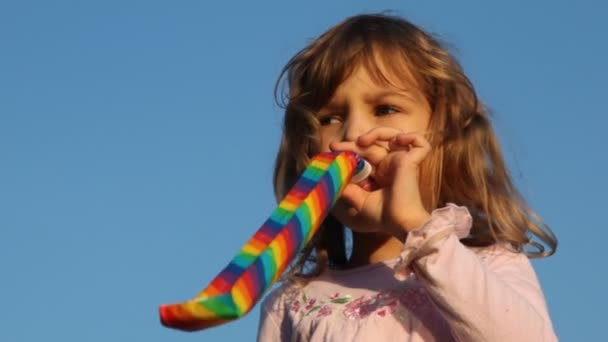 Little girl blows in party blower facing camera — Stock Video