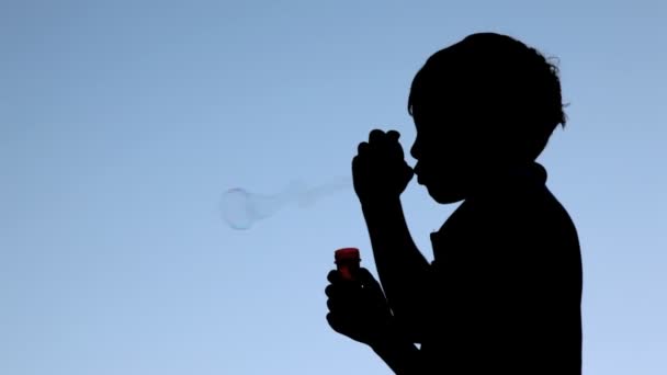 Silhouette of boy blowing up soap bubbles — Stock Video