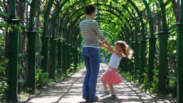 Madre e hija giran cogidas de la mano en plantas trenzadas corredor arqueado — Vídeo de stock