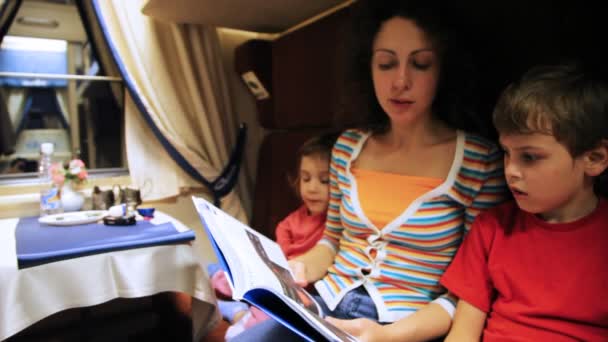 Mãe lê livro para filho e filha sentados no trem de equitação de cupê — Vídeo de Stock