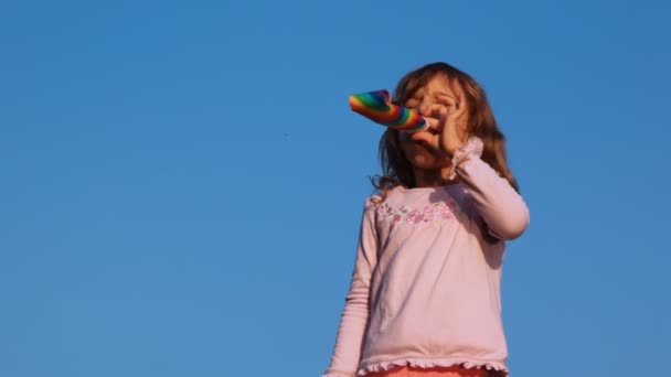 Niña sopla en soplador de fiesta en el cielo — Stok video