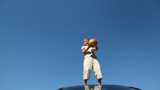 Boy stands on roof of car and throws up ball — Stock Video