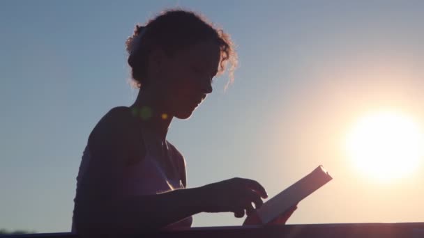 Kadının üzerinde sayfaları çevirme ve günbatımı gökyüzü karşı kitap okuma — Stok video