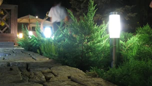 Las lámparas iluminan la terraza con las personas que pasan — Vídeo de stock