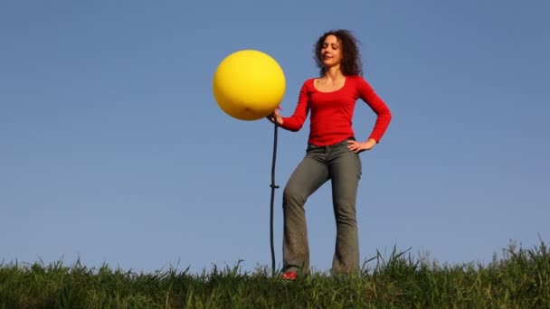 Girl stands in meadow and blows up foot pump balloon — Stock Video