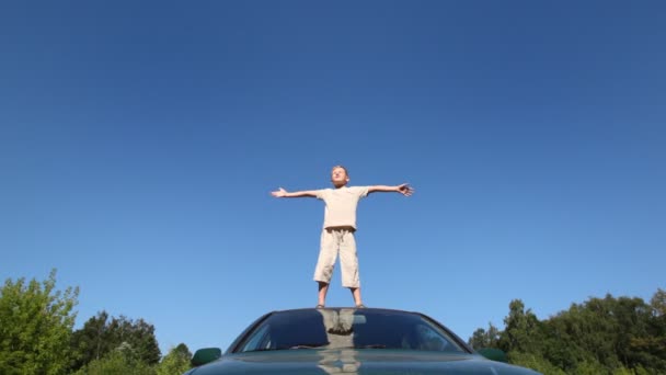 Pojke står på taket av passagerarebil med händerna brett isär — Stockvideo