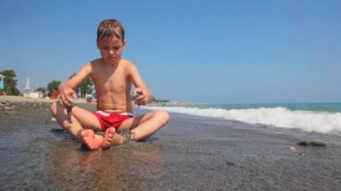 Çocuk deniz kenarında oturur ve kum ile oynuyor