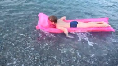 Çocuk pembe hava yatakta deniz aşağıya doğru yüzüyor.