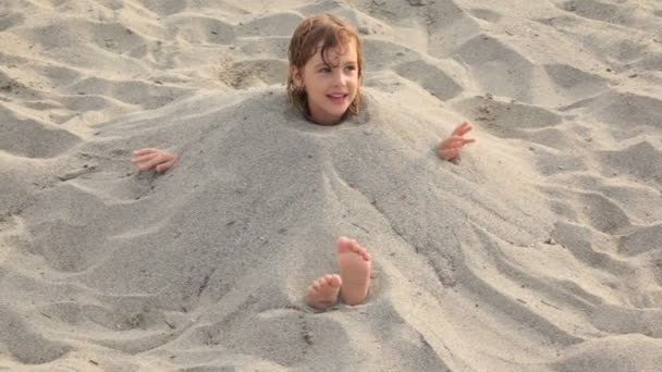 Menina senta-se cheio de areia no pescoço na praia — Vídeo de Stock