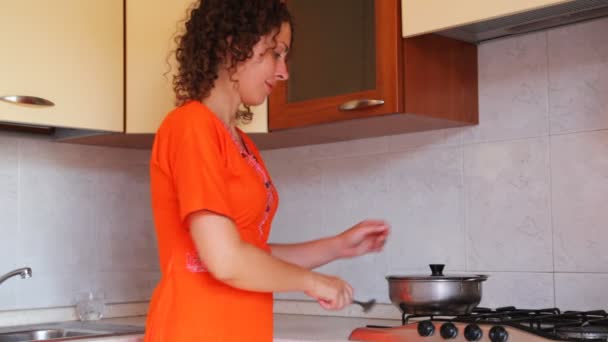 Girl at kitchen interferes with spoon in saucepan on stove — Stock Video