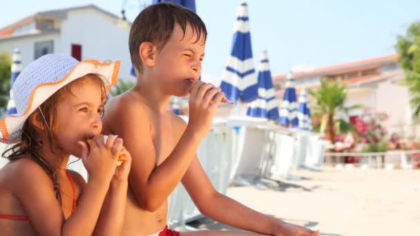 Chlapec a dívka jíst zmrzlinu na pláži, pak si olizuje ruku — Stock video