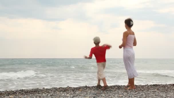 Mother and son stand on sea coast and throw pebbles — Stock Video