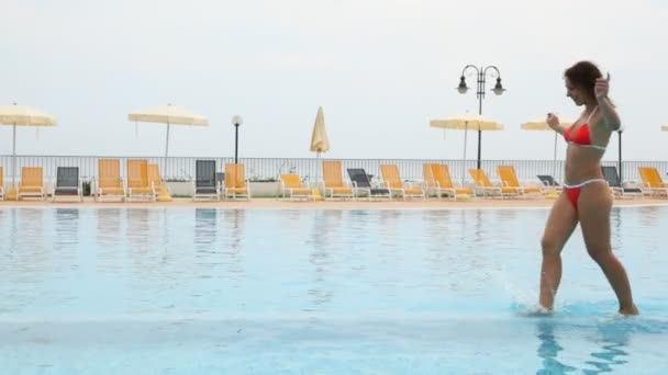 Mulher correr ao longo da piscina na frente de chaise longue e guarda-chuva de praia — Vídeo de Stock