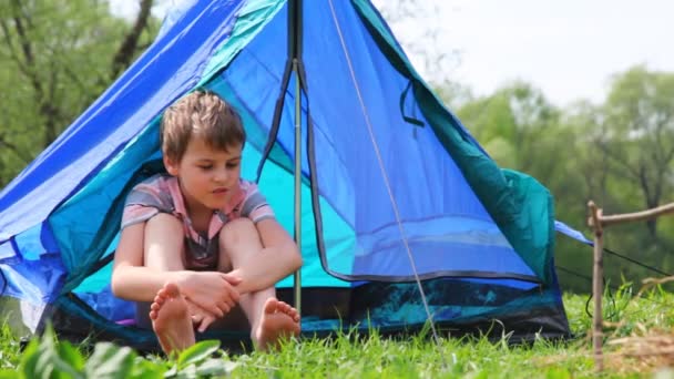 Ragazzo con i piedi nudi si siede in tenda nella foresta — Video Stock