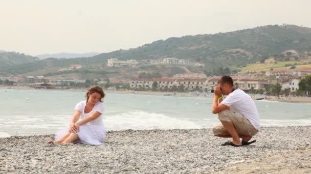 Мужчина в шортах фотографировал женщину на скалистом пляже — стоковое видео