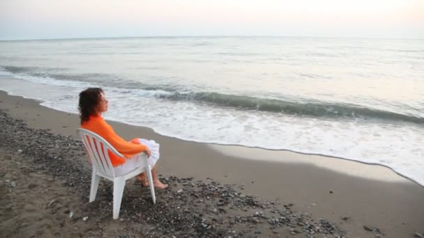 Woman sits on chair alone on beach and looks in distance pensive — Stock Video