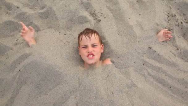 Top view head of boy lies smiles buried up with sand — Stock Video