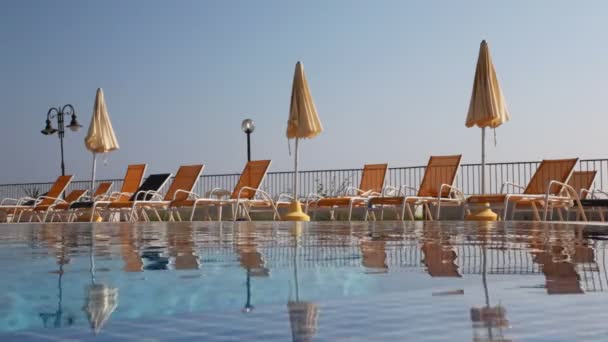 Camas de sol e guarda-sóis por piscina com água — Vídeo de Stock