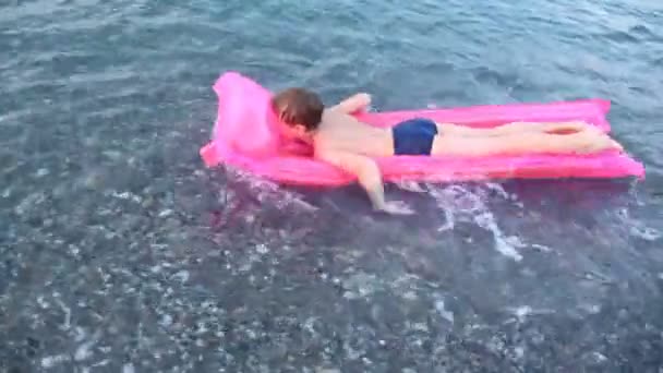 Jongen zweeft op roze lucht bed door zee naar beneden — Stockvideo